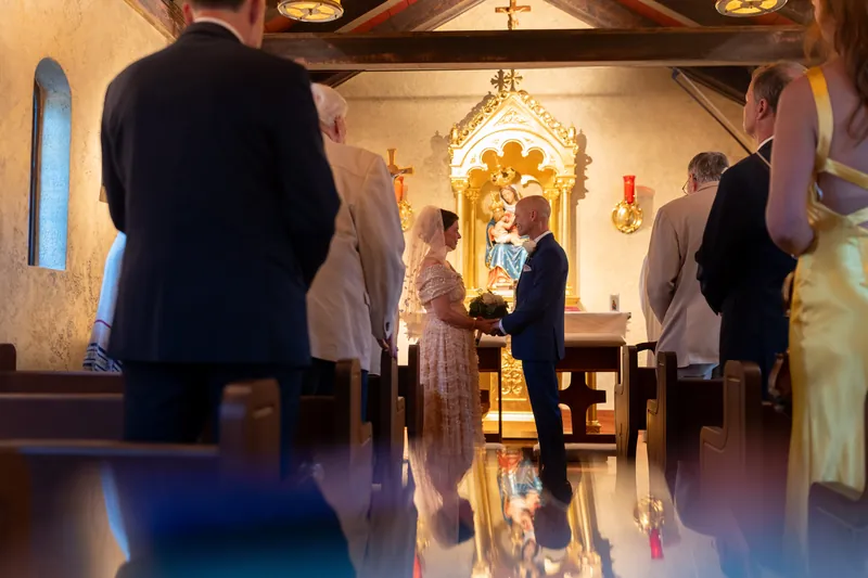 Bridgid in cream lace and Dan in a dark suit stand together as their ceremony concludes in the candlelit chapel.