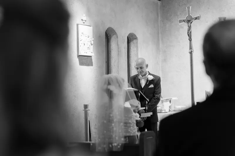 A priest in a dark suit reads from a book during a wedding ceremony at the shrine's altar.