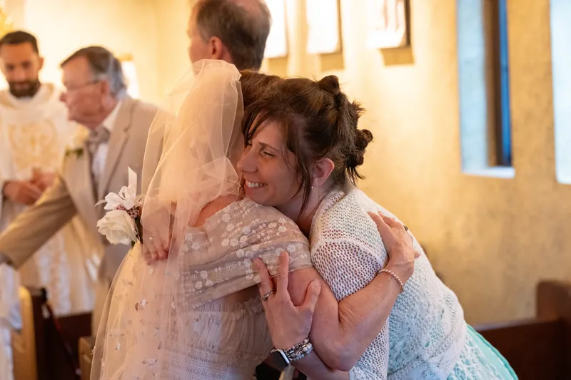 Bridgid embraces a family member inside the shrine's warm, candlelit interior while guests gather nearby.