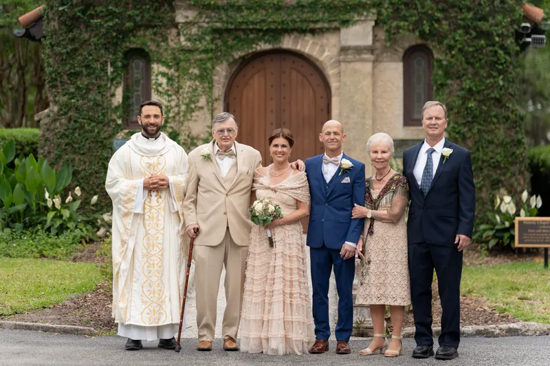 Wedding party and family members line up in front of the historic stone chapel with its ivy-draped facade and wooden door.