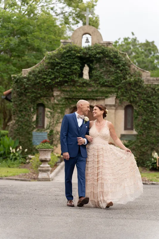 Dan and Bridgid stroll across the grounds with the stone chapel and bell tower behind them.
