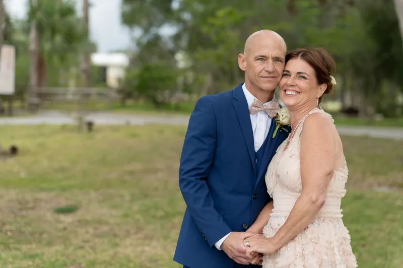 Dan and Bridgid embrace on the Mission grounds with crosses and trees in the background.