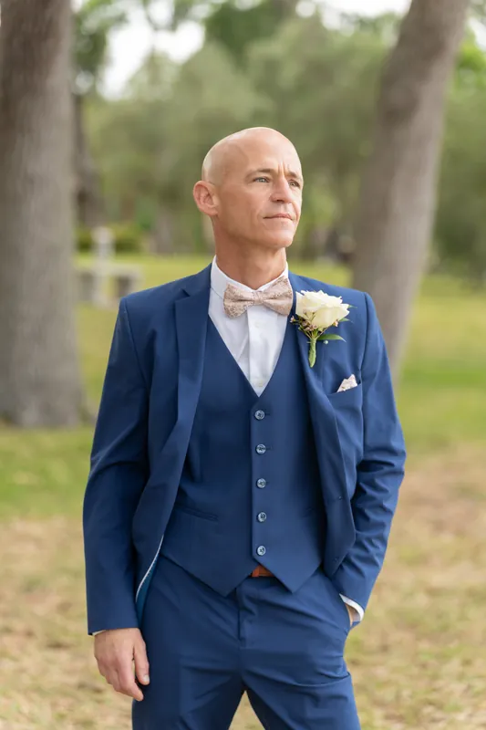 Dan stands in a navy three-piece suit with a white boutonnière, framed by moss-draped trees.