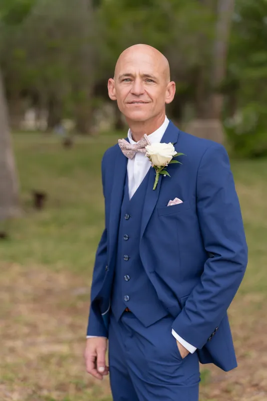 Dan smiles in profile wearing his navy suit and pale tie with a white flower pin at the shrine.