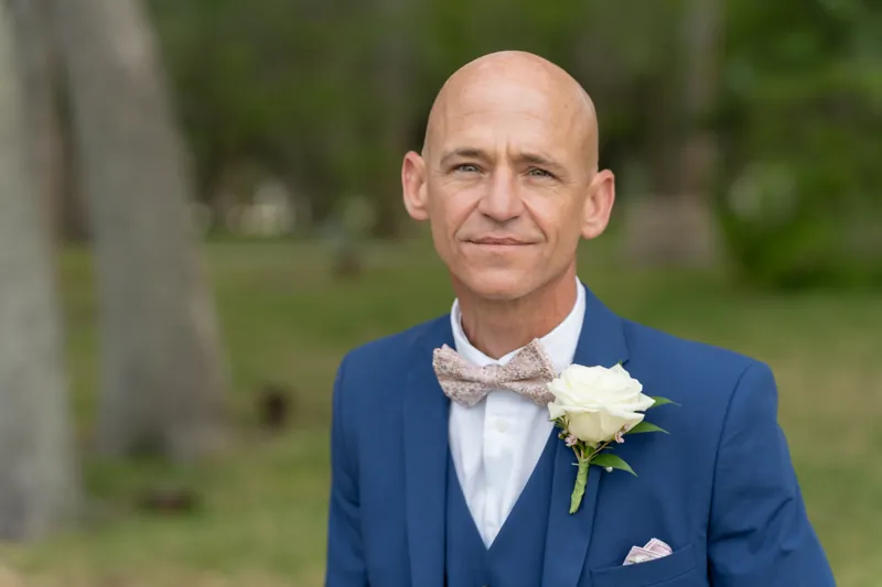 Dan faces the camera in his navy suit and gray tie, white boutonnière visible on his lapel.