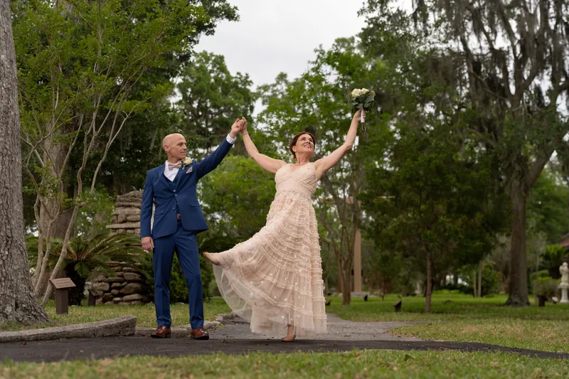 Dan raises Bridgid's arm as she spins beside an old wooden structure framed by draped oak branches.