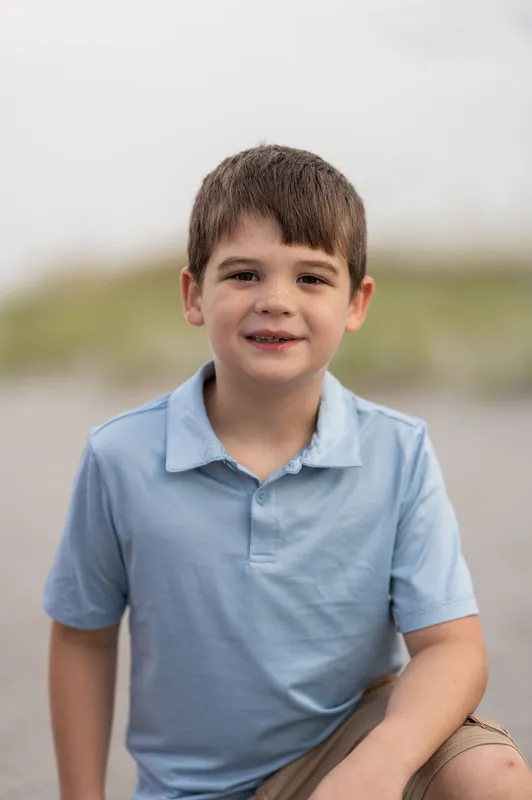 Young boy in light blue polo shirt smiles at the camera at Vilano Beach.