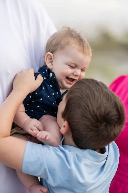 Their toddler laughs while being held up by Josh, with Brook's arm around them both.