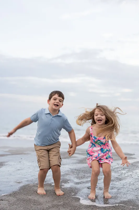 Two children laugh and run barefoot across the beach, their joy evident as they play near the ocean at Vilano Beach.