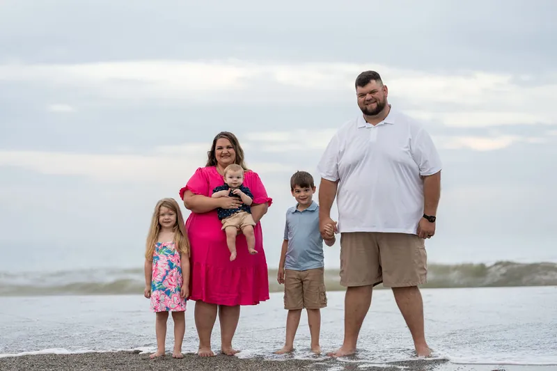Brook & Josh wade in the shallow surf with all three of their children lined up beside them at the water's edge.
