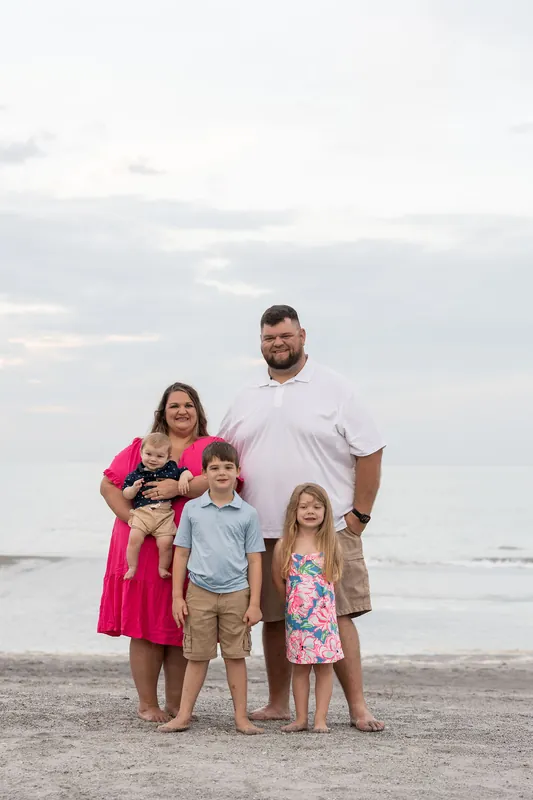 Four adults and two children stand together on Vilano Beach with calm water and overcast sky behind them, dressed in casual
