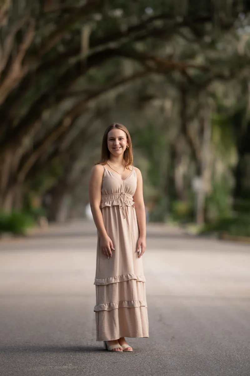 Full-length portrait of older sister in tiered maxi dress under oak trees