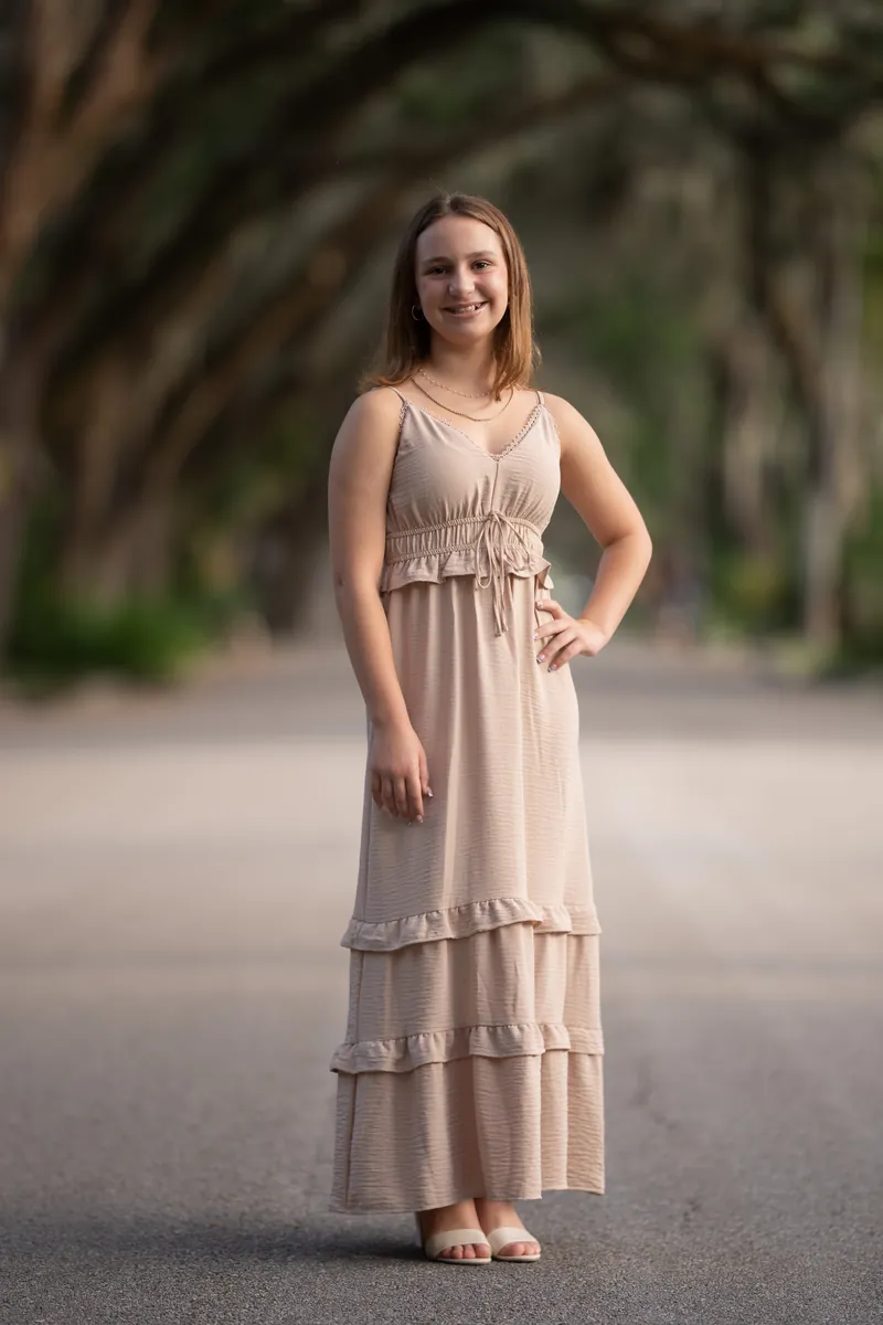 Older sister with hand on hip, smiling under oak canopy