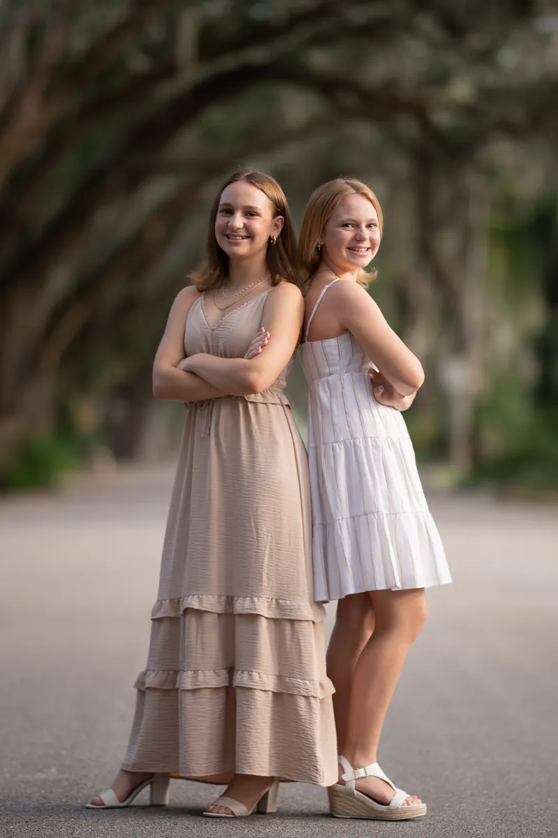 Two sisters standing back-to-back with arms crossed, smiling