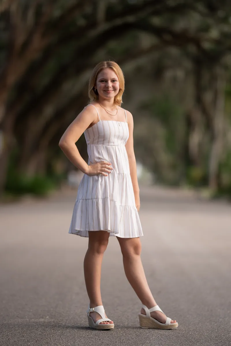 Younger sister in white sundress under oak canopy