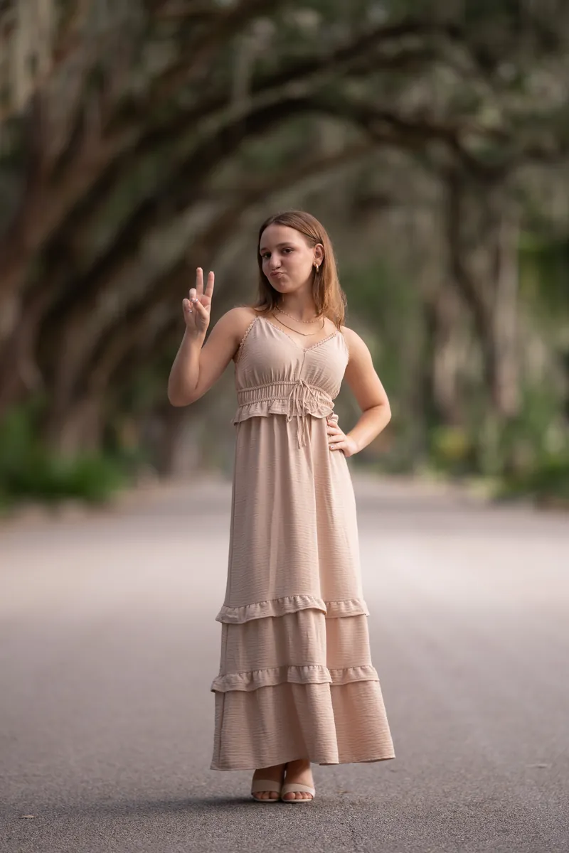 Teenage girl making peace sign with playful expression under oak canopy on Magnolia Street