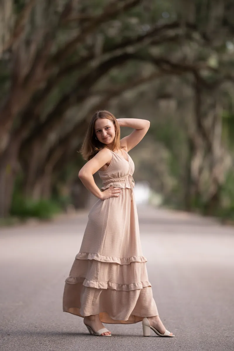 Older sister posing with hand behind head under oak trees