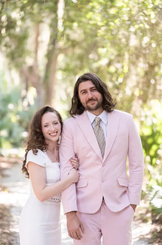 Cameron and Chris stand together on the boardwalk path, with Chris in a white dress holding Cameron's arm.
