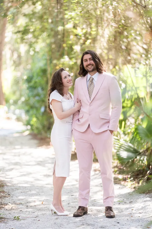 Cameron and Chris stand still on the boardwalk, holding hands and looking at each other amid the leafy canopy.