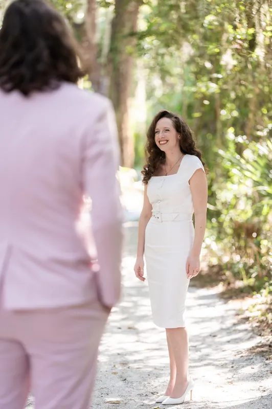 Two people face each other on a shaded path, one in pink suit and one in white dress at Fort Mose.