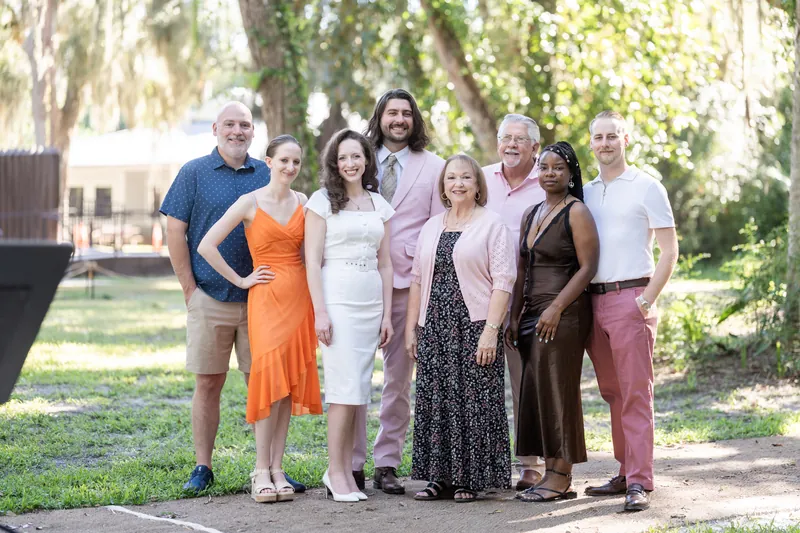 Eight family members stand together on the boardwalk path in mixed casual and formal attire at Fort Mose.