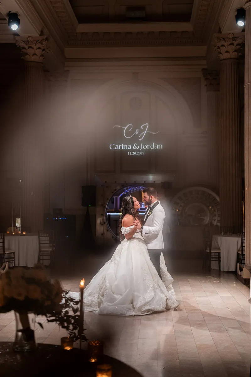 Carina and Jordan dance under uplighting with their monogram projected above them.