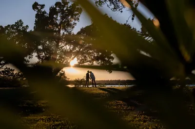 Carli and Jeff kiss silhouette framed through leaves at sunset at Washington Oaks Gardens State Park