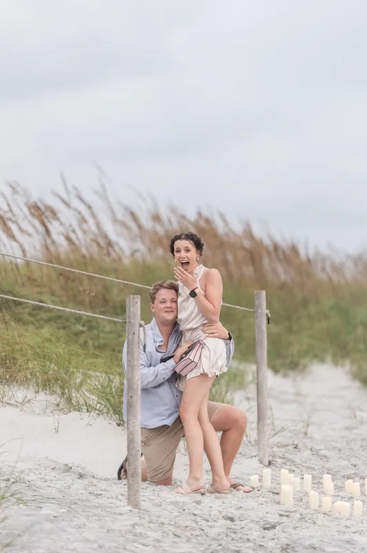 Carter and Emily stand together near the wooden dune fence, Emily's hand near her face with a joyful expression as she gazes at Carter.