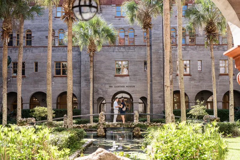 The Lightner Museum Courtyard showcases its symmetrical stone facade, tall palms, and central water feature under bright afternoon sunlight.