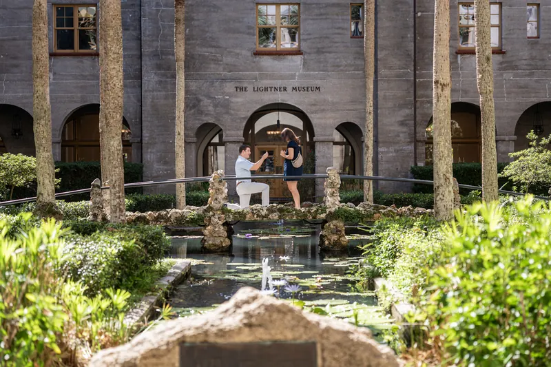 Casey and Amanda stand facing each other in the Lightner Museum courtyard, surrounded by manicured hedges and stone columns.