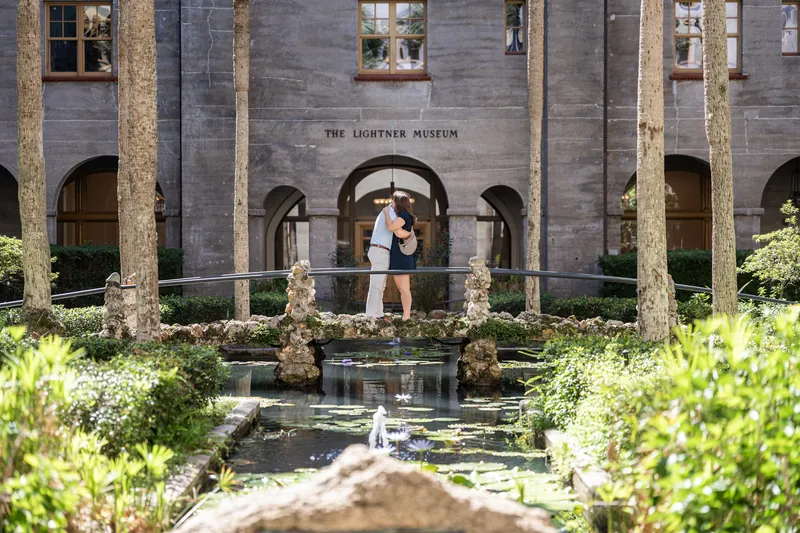 A couple stands together on the courtyard's stone pathway with classical architecture and lush greenery framing the scene.