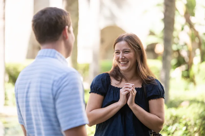A person in a light blue striped shirt smiles while speaking to someone in a dark navy dress under the museum's covered colonnade.