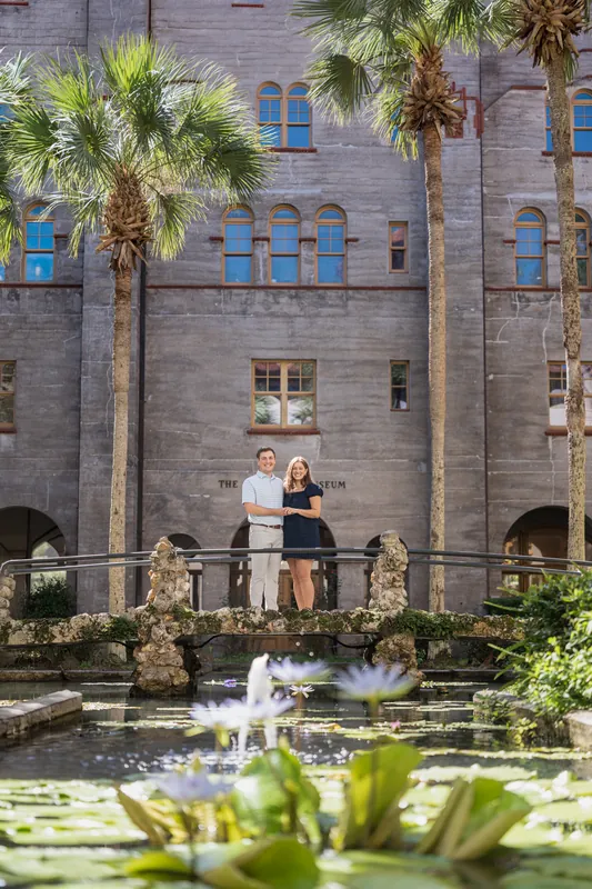 Casey and Amanda stand on a stone balcony overlooking a fountain at the Lightner Museum Courtyard, surrounded by palm trees and historic architecture.