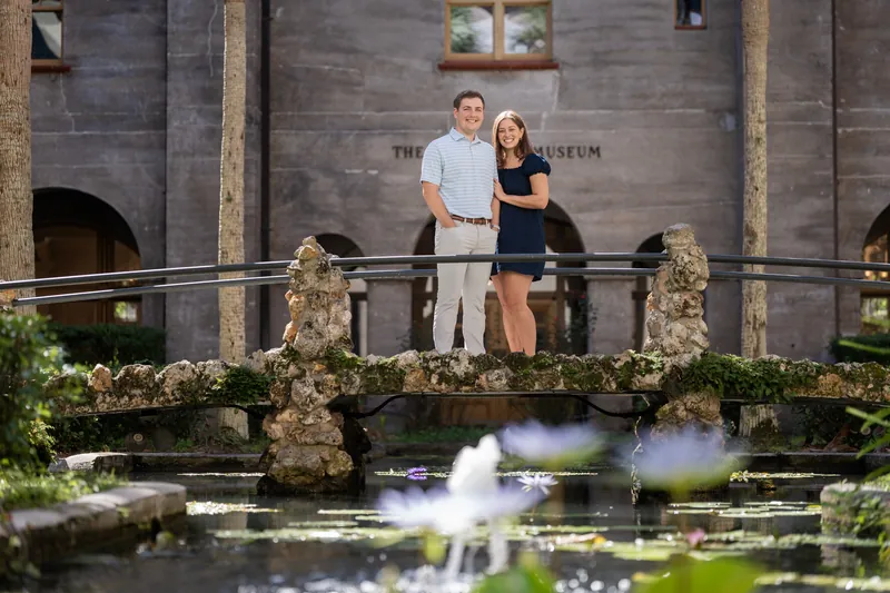 The couple poses together on a railed terrace with a fountain in the foreground and the museum's stone facade behind them.