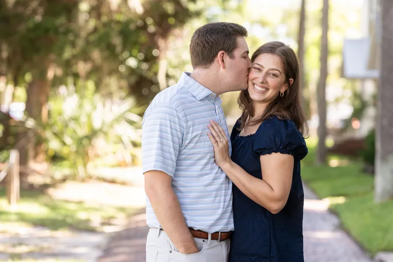 Casey and Amanda embrace on a tree-lined path in Downtown St Augustine, both smiling brightly.
