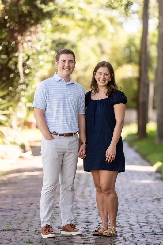Casey and Amanda hold hands while walking down a brick-lined street shaded by trees.