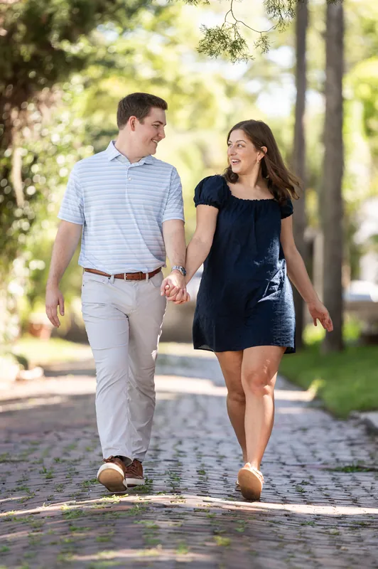 Casey and Amanda walk hand-in-hand down a brick pathway, their expressions joyful and relaxed.