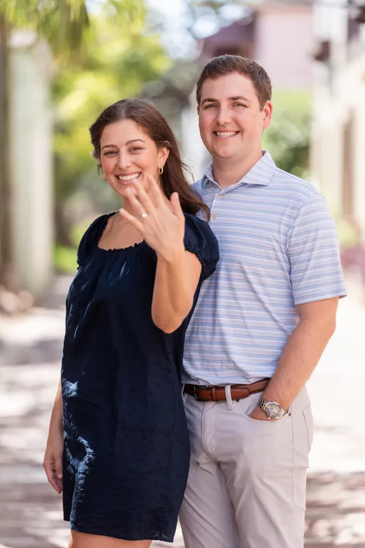 Casey and Amanda stand together on a tree-lined street in downtown St Augustine, smiling as she displays her engagement ring.