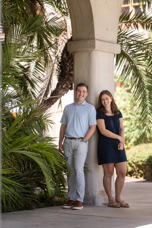 Beneath arched columns framed by palm fronds, two people stand hand-in-hand in the museum's covered walkway.