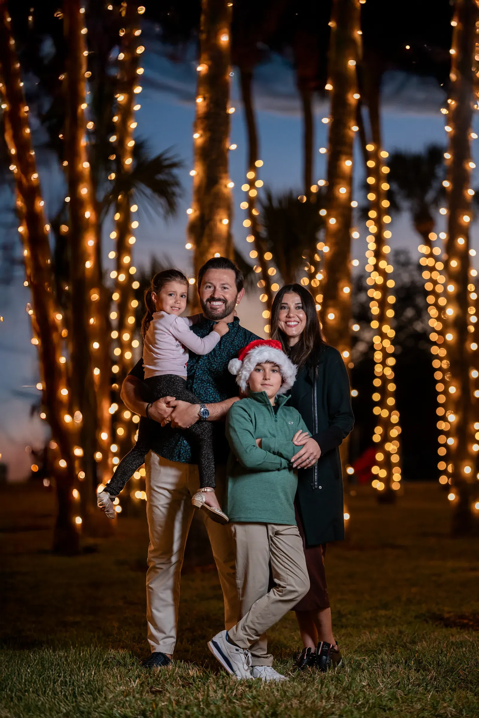 Family portrait with palm trees wrapped in holiday lights at sunset during St. Augustine Nights of Lights