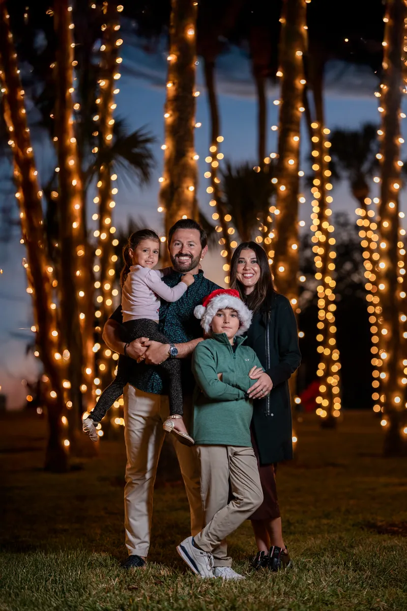 Family of four poses under illuminated palm trees at twilight