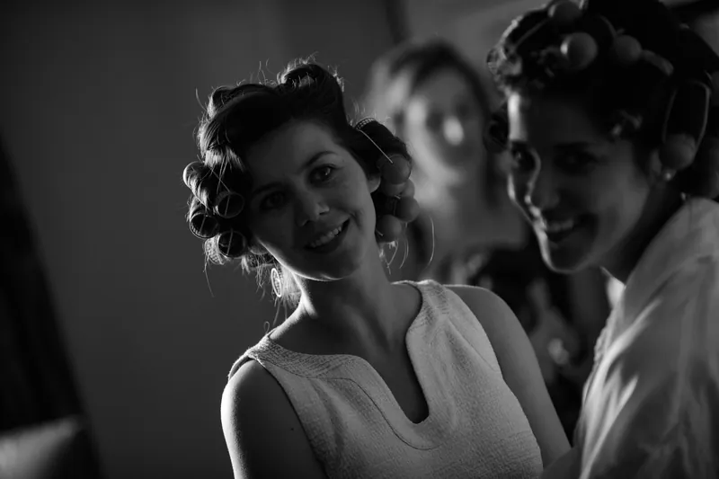 Choko smiles at the camera while surrounded by bridesmaids getting ready indoors, captured in black and white.