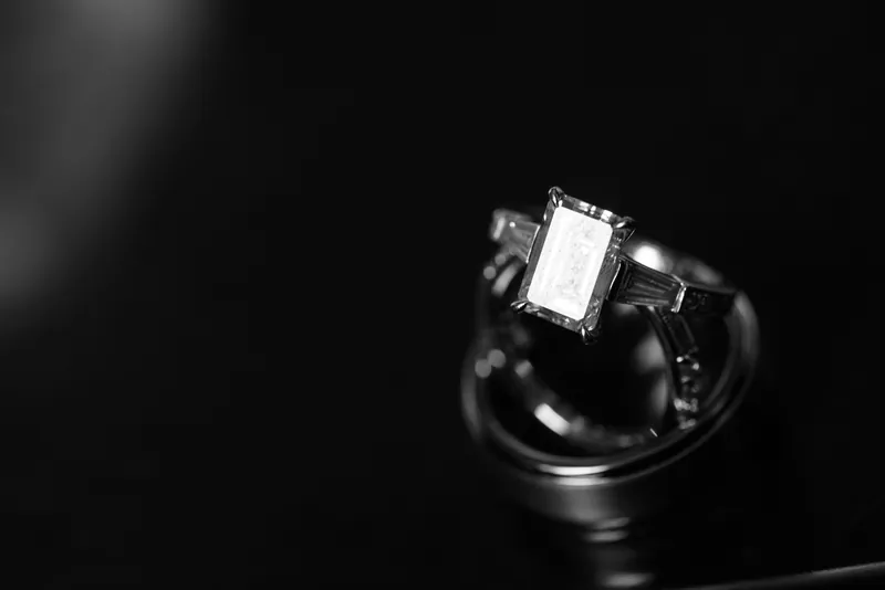 Choko's emerald engagement ring catches light against dark fabric in a close-up shot.