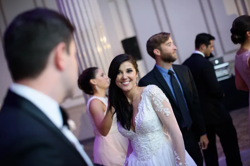 Choko in her beaded white gown stands smiling amid guests in formal wear at an indoor reception venue.