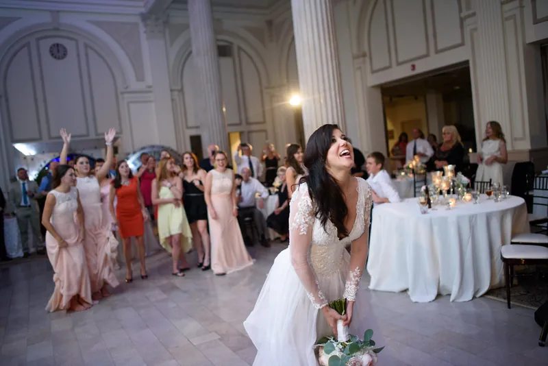 Choko walks across the elegant ballroom floor in her white gown as wedding guests mingle.