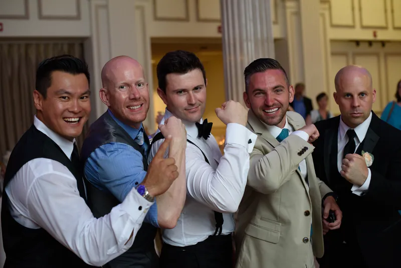 Five groomsmen flex playfully for the camera in dress shirts and vests at The Treasury on the Plaza.