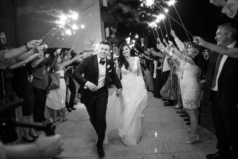 Choko and Michael run through a sparkler-lined tunnel as wedding guests wave sparklers at The Treasury on the Plaza in St.