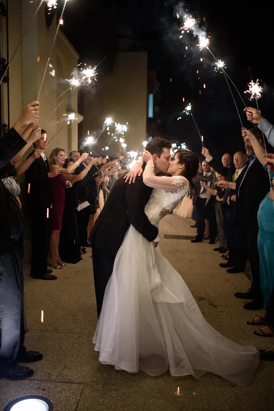 Michael lifts Choko high as guests on either side hold glowing sparklers during their exit at The Treasury on the Plaza