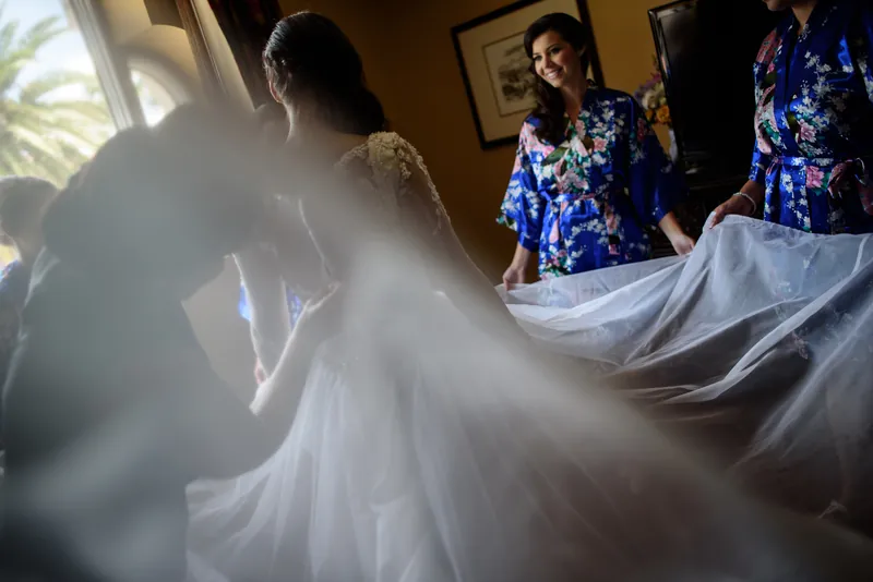 Sunlight streams across Choko's flowing white gown as bridesmaids in blue sequined dresses help arrange her train.