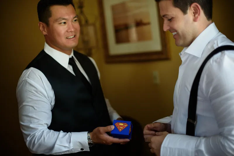 Michael holds a blue ring box while exchanging a smile with another man in formal attire at Casa Monica Resort & Spa.
